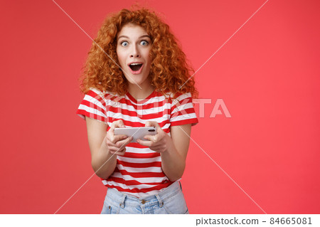 Impressed excited good-looking redhead curly woman hold smartphone horizontal open mouth fascinated stare camera thrilled astonished win passed level game happy playing cool app red background Impressed excited good-looking redhead curly woman hold smartphone horizontal open mouth fascinated stare camera thrilled astonished win passed level game happy playing cool app red background 84665081