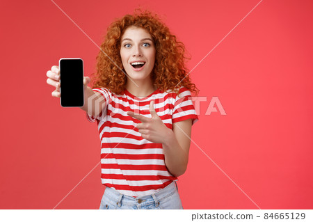 Take look what awesome smartphone. Impressed excited good-looking female love digital innovations redhead girl curly hairstyle showing phone screen pointing display promote cool app Take look what awesome smartphone. Impressed excited good-looking female love digital innovations redhead girl curly hairstyle showing phone screen pointing display promote cool app 84665129