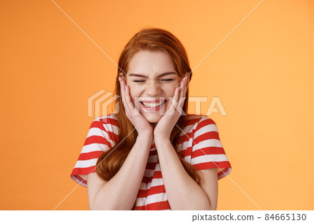 Close-up cheerful lucky excited smiling girl, cannot believe cheering hear excellent news, close eyes celebrating, touch cheeks blushing joy delight, rejoicing awesome situation, orange background Close-up cheerful lucky excited smiling girl, cannot believe cheering hear excellent news, close eyes celebrating, touch cheeks blushing joy delight, rejoicing awesome situation, orange background 84665130