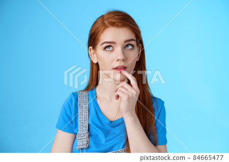 Close-up curious dreamy creative redhead female working project, student thinking essay, touch lip intrigued, look up thoughtful, pondering choice, make assumptions, stand blue background 84665477