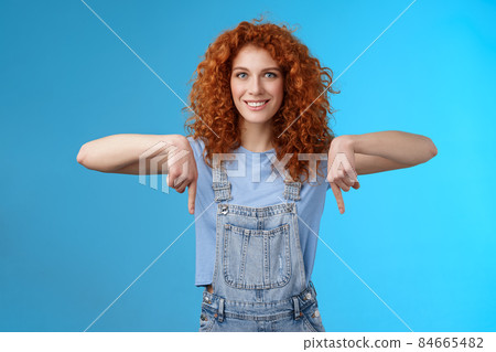 Charismatic sassy flirty redhead daring ginger girl curly haircut pointing down index fingers smiling broadly enthusiastic explore new store pointing promo like cool advertisement blue background Charismatic sassy flirty redhead daring ginger girl curly haircut pointing down index fingers smiling broadly enthusiastic explore new store pointing promo like cool advertisement blue background 84665482
