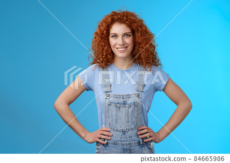 Attractive sassy motivated redhead european female curly-haired hold hands waist empowered express confidence self-assured look forward ready win conqueror, stand blue background 84665986