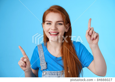 Close-up cheerful carefree redhead dancing girl pointing up, raising fingers, smiling amused, having fun, stand blue background entertained, enjoy music party, disco mood, carefree emotions concept 84666027