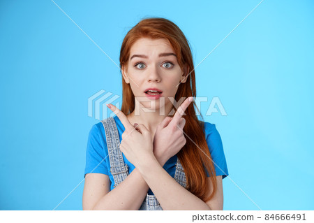 Questioned ambushed cute redhead woman asking advice picking product, cross hands pointing sideways, show left right choices, look camera wondered uncertain, making decision, blue background Questioned ambushed cute redhead woman asking advice picking product, cross hands pointing sideways, show left right choices, look camera wondered uncertain, making decision, blue background 84666491