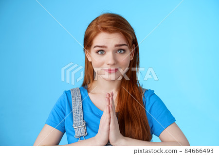 Close-up attractive tender redhead woman asking pretty please, supplicating, hold hands pray, namaste gesture, look sincere pity, smiling begging help favor, stand blue background 84666493