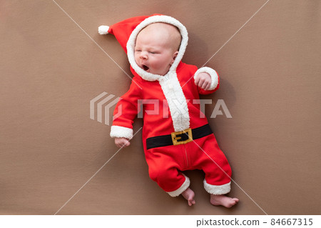 Newborn girl dressed in santa claus costume yawning being tired. Newborn girl dressed in santa claus costume yawning being tired. 84667315