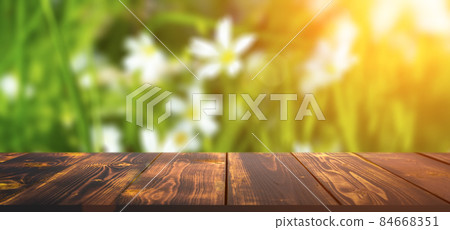 Forest wooden table background. Summer sunny meadow with green grass, forest trees background and rustic wooden surface for goods, products, food Forest wooden table background. Summer sunny meadow with green grass, forest trees background and rustic wooden surface for goods, products, food 84668351