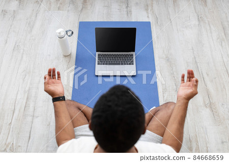 Millennial african american guy look at laptop with empty screen on mat on floor with bottle of water Millennial african american guy look at laptop with empty screen on mat on floor with bottle of water 84668659