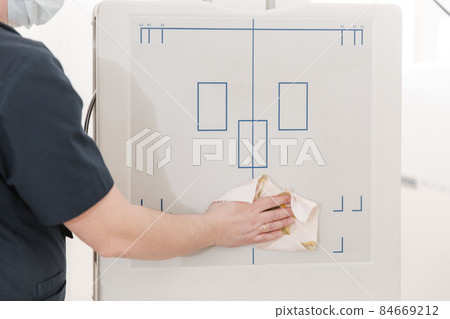 Doctor cleans the X-ray machine. X-ray department in modern hospital. Radiology room with scan machine with empty bed. Technician adjusting an x-ray machine. Doctor cleans the X-ray machine. X-ray department in modern hospital. Radiology room with scan machine with empty bed. Technician adjusting an x-ray machine. 84669212