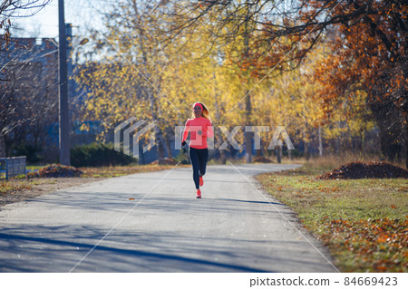 Young fitness woman running on the road in the cold morning in winter. Young fitness woman running on the road in the cold morning in winter. 84669423