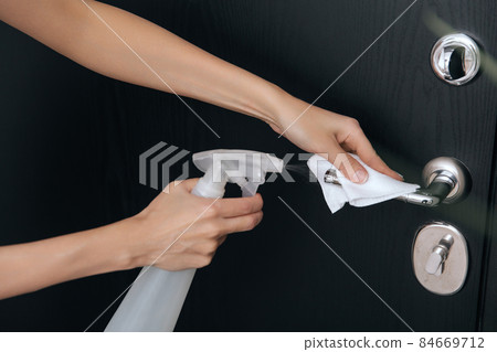 Cleaning black door handles with an antiseptic wet wipe and sanitizer spray. Disinfection in hospital and public spaces against corona virus. Woman hand using towel for cleaning home room door link. 84669712
