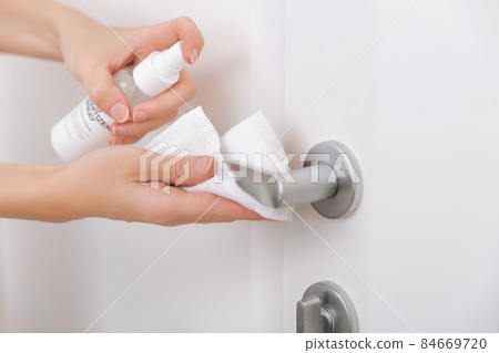 Cleaning white door handles with an antiseptic wet wipe and sanitizer spray. Disinfection in hospital and public spaces against corona virus. Woman hand using towel for cleaning home room door link. Cleaning white door handles with an antiseptic wet wipe and sanitizer spray. Disinfection in hospital and public spaces against corona virus. Woman hand using towel for cleaning home room door link. 84669720