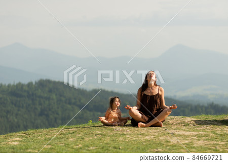 Mother in pose of lotus in mountains with little daughter. Mother in pose of lotus in mountains with little daughter. 84669721