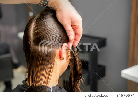 Hairdresser divides female hair into sections with comb holding hair with her hands in hair salon close up. Hairdresser divides female hair into sections with comb holding hair with her hands in hair salon close up. 84670674