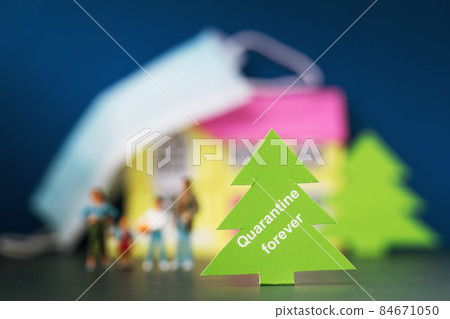 Christmas tree made of paper with text on the background of a blurred toy house, people and a medical mask, the concept of quarantine forever Christmas tree made of paper with text on the background of a blurred toy house, people and a medical mask, the concept of quarantine forever 84671050