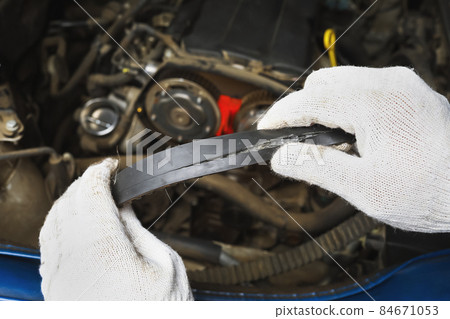 An auto mechanic shows a timing belt burst from the back side, close-up 84671053