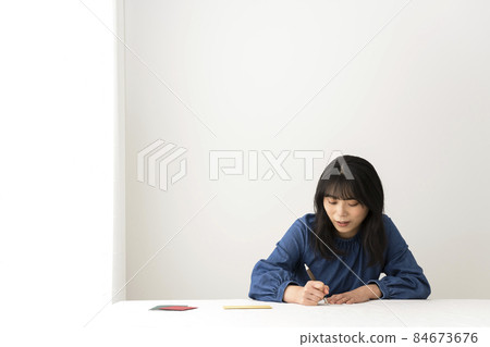 A woman writing a message card to give with a gift at the desk A woman writing a message card to give with a gift at the desk 84673676