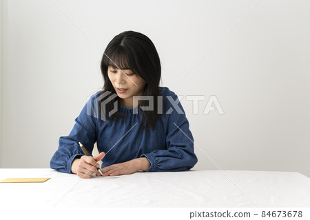 A woman writing a message card to give with a gift at the desk 84673678