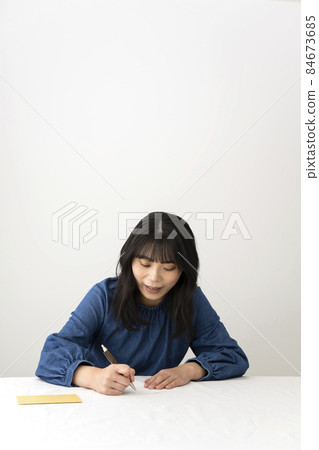 A woman writing a message card to give with a gift at the desk 84673685