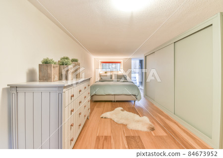 Minimalist interior design of small bedroom with soft bed placed in corner and wooden wardrobe and shelves with lamp illumination 84673952