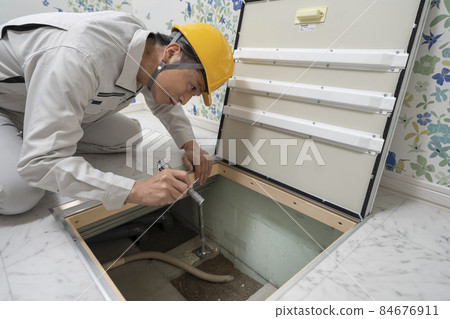 A man in work clothes looking inside from the underfloor inspection door of a house A man in work clothes looking inside from the underfloor inspection door of a house 84676911