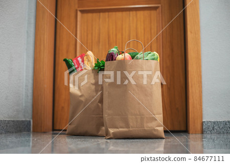 Food shopping bags stand at the door of the house or apartment. Vegetables and fruits delivery during quarantine and self-isolation. Food shopping bags stand at the door of the house or apartment. Vegetables and fruits delivery during quarantine and self-isolation. 84677111
