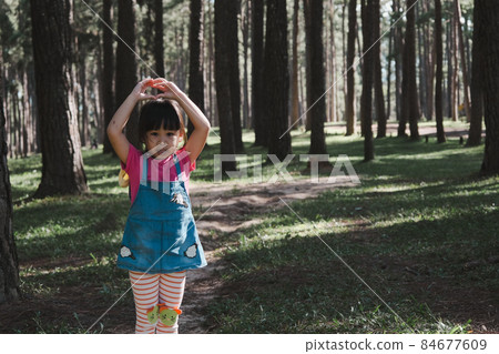 Active little girls running in the pine forest on a warm summer day. Happy girl smiles and laughs while spending time with her family in the park on vacation. 84677609