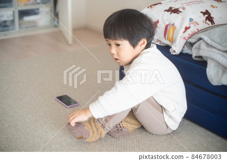 A 4-year-old child wearing socks while talking on a smartphone in a sunny room 84678003