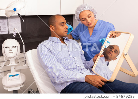 Cosmetologist examining male client face before procedure Cosmetologist examining male client face before procedure 84679282