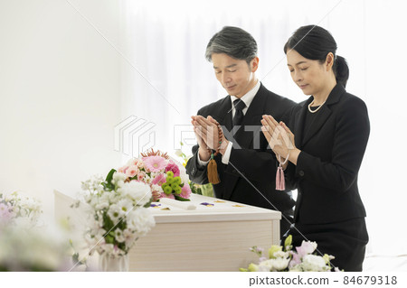 Men and women in mourning holding beads and holding hands in front of the casket 84679318
