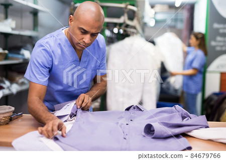 Confident man dry-cleaning worker checking clean clothes 84679766