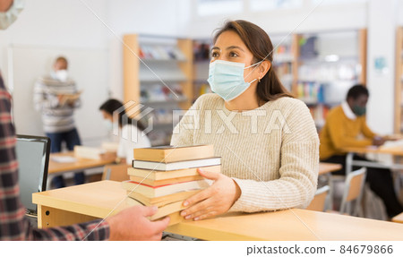 Woman in mask returning books at library Woman in mask returning books at library 84679866