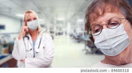 Senior Adult Female Looking Down as Doctor Stands Behind All Wearing Medical Face Masks Within Hospital. Senior Adult Female Looking Down as Doctor Stands Behind All Wearing Medical Face Masks Within Hospital. 84680318