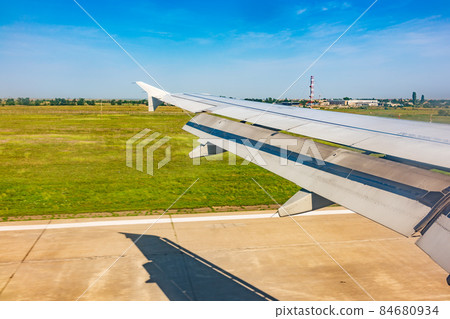 View of airplane wing, blue skies and green land with plane shadow during landing. Airplane window view. 84680934