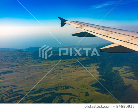 View of airplane wing, blue skies and green land during landing. Airplane window view. 84680935