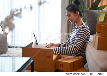 Happy young woman working with laptop in her home office. Startup small business SME concept. Happy young woman working with laptop in her home office. Startup small business SME concept. 84682008