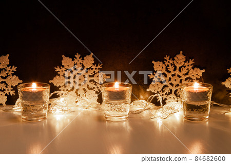 Composition of three burning candles, snowflakes and fairy lights in form of stars Composition of three burning candles, snowflakes and fairy lights in form of stars 84682600