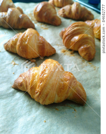 Freshly baked croissants on a baking tray with parchment paper. Freshly baked croissants on a baking tray with parchment paper. 84682777