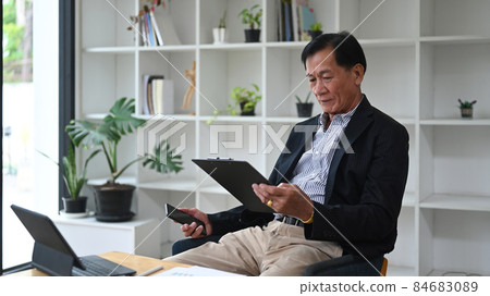 Mature businessman working with computer tablet and analyzing financial reports in office. 84683089