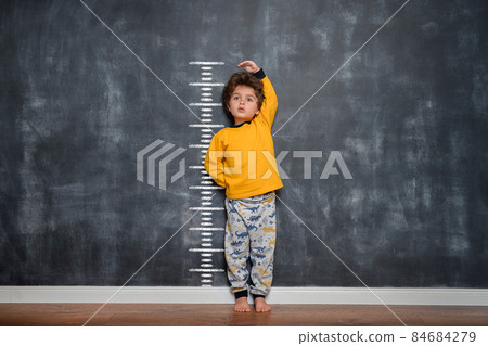 Funny little child measuring his height near blackboard wall. Kindergarten or school concept. Kid ready to study 84684279