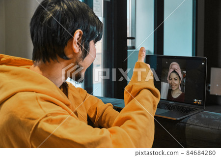 An Asian guy sits in a small office, communicates via laptop with his girlfriend An Asian guy sits in a small office, communicates via laptop with his girlfriend 84684280