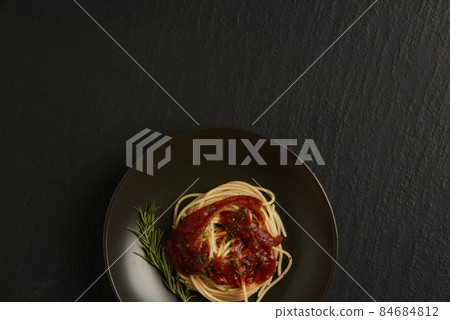pasta concept a dish of boiled long slim pasta with red sauce being served on the black table together with a wooden spoon and fork 84684812