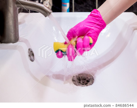 A hand in a pink glove washes a washbasin in the bathroom with a sponge with detergent. 84686544