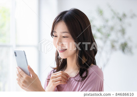 A woman who wears a loungewear and operates a smartphone 84686610