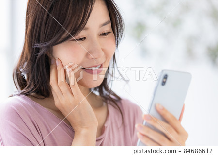 A woman who wears a loungewear and operates a smartphone 84686612