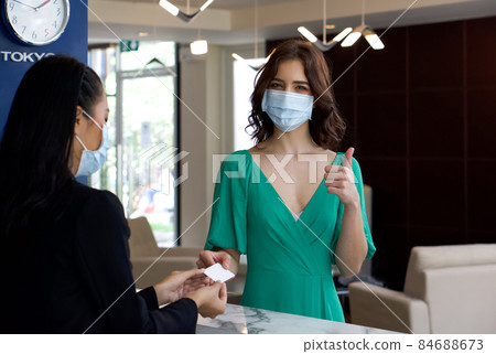 Caucasian tourist in green cloth  receiving a room card from hotel manager in black suit. Hotel staff and tourist wear face mask to protect them from the coronavirus outbreak. 84688673
