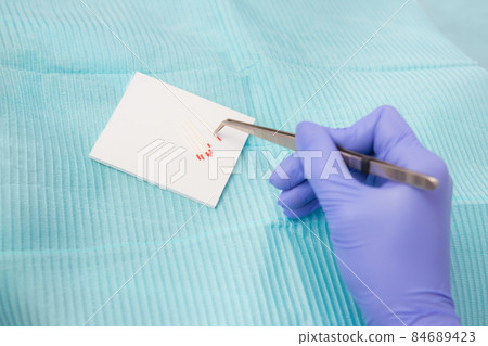 gutta-percha pins in a set of different sizes for filling root canals, one pin in close-up in dental tweezers, material for endodontic fillings. dentist in blue gloves gutta-percha pins in a set of different sizes for filling root canals, one pin in close-up in dental tweezers, material for endodontic fillings. dentist in blue gloves 84689423