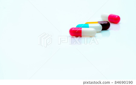 Multi-color antibiotic capsule pills on white background. Selective focus on pink and white capsule pill. Antibiotic drug resistance. Prescription drugs. Pharmaceutical industry. Antimicrobial drugs. Multi-color antibiotic capsule pills on white background. Selective focus on pink and white capsule pill. Antibiotic drug resistance. Prescription drugs. Pharmaceutical industry. Antimicrobial drugs. 84690190