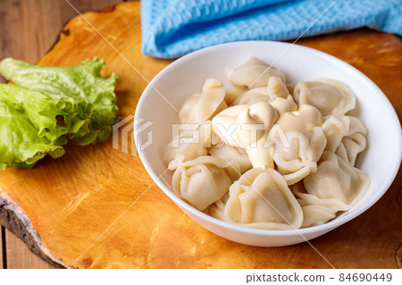 Dumplings in a white plate with salad on a wooden background. Dumplings in a white plate with salad on a wooden background. 84690449