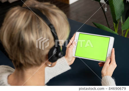 A middle-aged woman with a headset is viewing content using a tablet on a green screen, calling her relatives 84690679